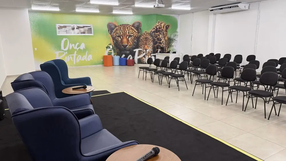 Sala de eventos com mural da onça pintada e cadeiras dispostas em fileiras